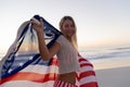 Caucasian woman holding and waving an US flag at the beach.