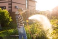 Caucasian woman gardener in work clothes watering the beds in her vegetable garden on sunny warm summer day. Concept of