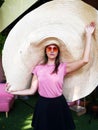 Caucasian woman in giant straw hat in sunglasses heart shape and pink t-shirt
