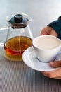 Caucasian woman hands hold ceramic cup with black tea and milk, glass teapot in background over metallic table Royalty Free Stock Photo