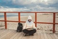 Caucasian woman in hat and jacket with backpack in winter sits on wooden pier on beach near North Sea. Denmark Royalty Free Stock Photo