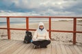 Caucasian woman in hat and jacket with backpack in winter sits on wooden pier on beach near North Sea. Denmark Copenhagen tourist Royalty Free Stock Photo