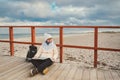 Caucasian woman in hat and jacket with backpack in winter sits on wooden pier on beach near North Sea. Denmark Copenhagen tourist Royalty Free Stock Photo