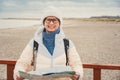 Caucasian woman in hat and jacket with backpack in winter sits on wooden pier on beach near North Sea. Denmark Copenhagen tourist Royalty Free Stock Photo