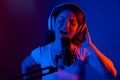 Caucasian woman in headphones singing into a microphone in neon light on a black background. An emotional girl is Royalty Free Stock Photo