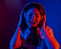 Caucasian woman in headphones singing into a microphone in neon light on a black background. An emotional girl is Royalty Free Stock Photo