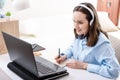 Caucasian woman with headphones writes in notebook, looks at laptop screen, remote work at home, home training Royalty Free Stock Photo