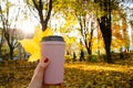 Caucasian woman holding cup of coffee with yellow maple leaf on the background of autumn landscape and rays of the sun. Cozy Royalty Free Stock Photo