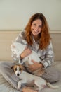 Caucasian woman holding a white fluffy cat and Jack Russell Terrier dog while sitting on the bed. The red-haired girl Royalty Free Stock Photo