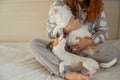 Caucasian woman holding a white fluffy cat and Jack Russell Terrier dog while sitting on the bed. The red-haired girl Royalty Free Stock Photo