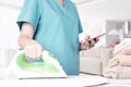 Caucasian woman, housewife, housekeeper, maid ironing clothes with an electric iron on an ironing board and looking at the screen Royalty Free Stock Photo