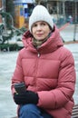 A Caucasian woman in a knitted hat and winter down jacket holds a paper cup of coffee in her hands Royalty Free Stock Photo