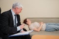 Caucasian woman lies on a couch at a reception with a psychotherapist. An elderly man works as a psychiatrist Royalty Free Stock Photo