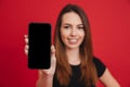 Caucasian woman with long brown hair doing commercial and presenting new mobile device in focus on camera, isolated over red back Royalty Free Stock Photo