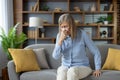 Caucasian woman with low immunity getting seasonal cold and sneezing in paper tissue at home. Mature lady trying to deal Royalty Free Stock Photo