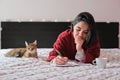 A caucasian woman lying on her bed writing with a cat by her side Royalty Free Stock Photo