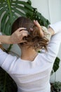 Caucasian woman making ponytail with beige scrunchie against bright, white background wall and monstera plant. View from the back Royalty Free Stock Photo