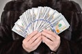 A caucasian woman in a mink coat holds many dollar bills in her hands. Front view from a low angle. No face Royalty Free Stock Photo