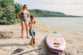 Caucasian woman mother teaching son to inflate sup surfboard with pump on beach.