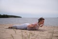 Caucasian woman practicing yoga, doing Salabhasana pose variation on beach