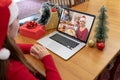 Caucasian woman in santa hat making christmas laptop video call with smiling family at dinner table Royalty Free Stock Photo