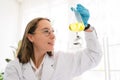 Caucasian woman scientist researcher wearing eye glasses shaking substance in the conical flask for analysis of liquids in the lab