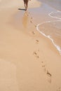 Caucasian woman seen from her back walking on an empty beach. Footprints in the sand. Circulatory system is improved by aerobic ex