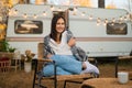 Caucasian woman sits in a wicker chair wrapped in a blanket in the yard near the trailer in autumn.