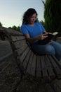 Caucasian woman sitting on a bench in the park reading a black book Royalty Free Stock Photo