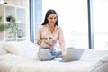 Caucasian woman sitting on comfy bed with wireless laptop, eating healthy salad Royalty Free Stock Photo