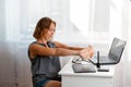 A caucasian woman sitting at a Desk doing a workout from fatigue. White window in the background. The concept of fatigue at work, Royalty Free Stock Photo