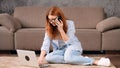 Caucasian woman sitting on the floor with her laptop and talking on the phone Royalty Free Stock Photo