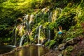 Woman sitting on the rock, practicing yoga. Young woman raising arms with namaste mudra near waterfall. Banyu Wana Amertha