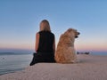 Caucasian woman sitting by the sea with her dog watching the sunrise Royalty Free Stock Photo