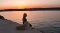 Caucasian woman sitting by the sea with her dog watching the sunset Royalty Free Stock Photo