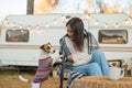 Caucasian woman sitting in a wicker chair wrapped in a blanket with a dog in the yard near the trailer in autumn.