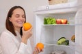 Caucasian woman standing taking some food from fridge filled with healthy vegetables and fruits while cooking at home smelling Royalty Free Stock Photo