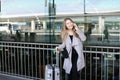 Caucasian woman standing with valise and talking by smartpone near airport. Royalty Free Stock Photo