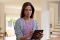 Caucasian woman staning in kitchen using digital tablet looking at camera and smiling