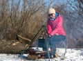 Caucasian woman warm hands by campfire, pot over bonfire on tripod, winter cooking at campsite, camping lifestyle