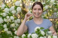 Caucasian woman takes an antihistamine medicine and removes a clothespin from her nose near a flowering tree.