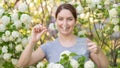 Caucasian woman takes an antihistamine medicine and removes a clothespin from her nose near a flowering tree.