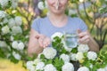 Caucasian woman takes an antihistamine medicine and removes a clothespin from her nose near a flowering tree.