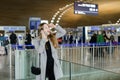 Caucasian woman talking by smartphone and looking for friend at aiport. Royalty Free Stock Photo