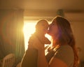 A Caucasian woman tenderly kisses her newborn son in the morning rays of sunlight.