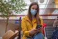 Caucasian woman tourist in waiting room with medical mask protection work in smartphone. Travaler woman in yellow with Royalty Free Stock Photo