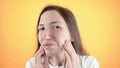 Caucasian woman with upset face shows with her hands on problem skin, acne, close up  on yellow wall. Royalty Free Stock Photo