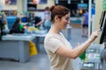 Caucasian woman uses a self-checkout counter. Self-purchase of groceries in the supermarket without a seller Royalty Free Stock Photo