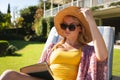 Caucasian woman wearing sunhat and sunglasses relaxing in sunny garden holding book Royalty Free Stock Photo
