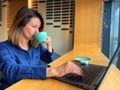 Caucasian woman working online browsing on laptop while drinking coffee sitting in cafe. Female professional typing on Royalty Free Stock Photo